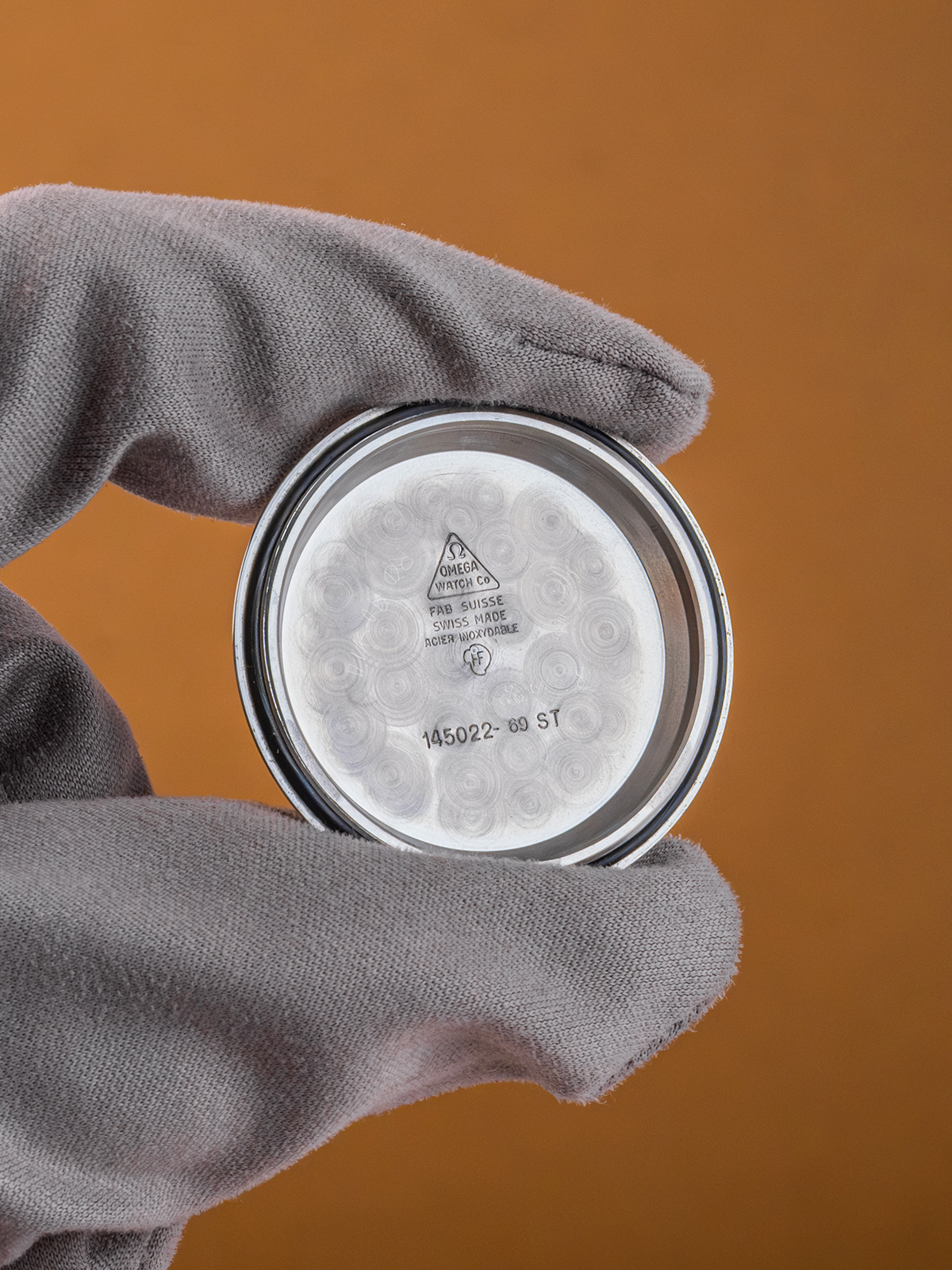 Hand wearing a gray glove holding a metallic container lid with a label against an orange background