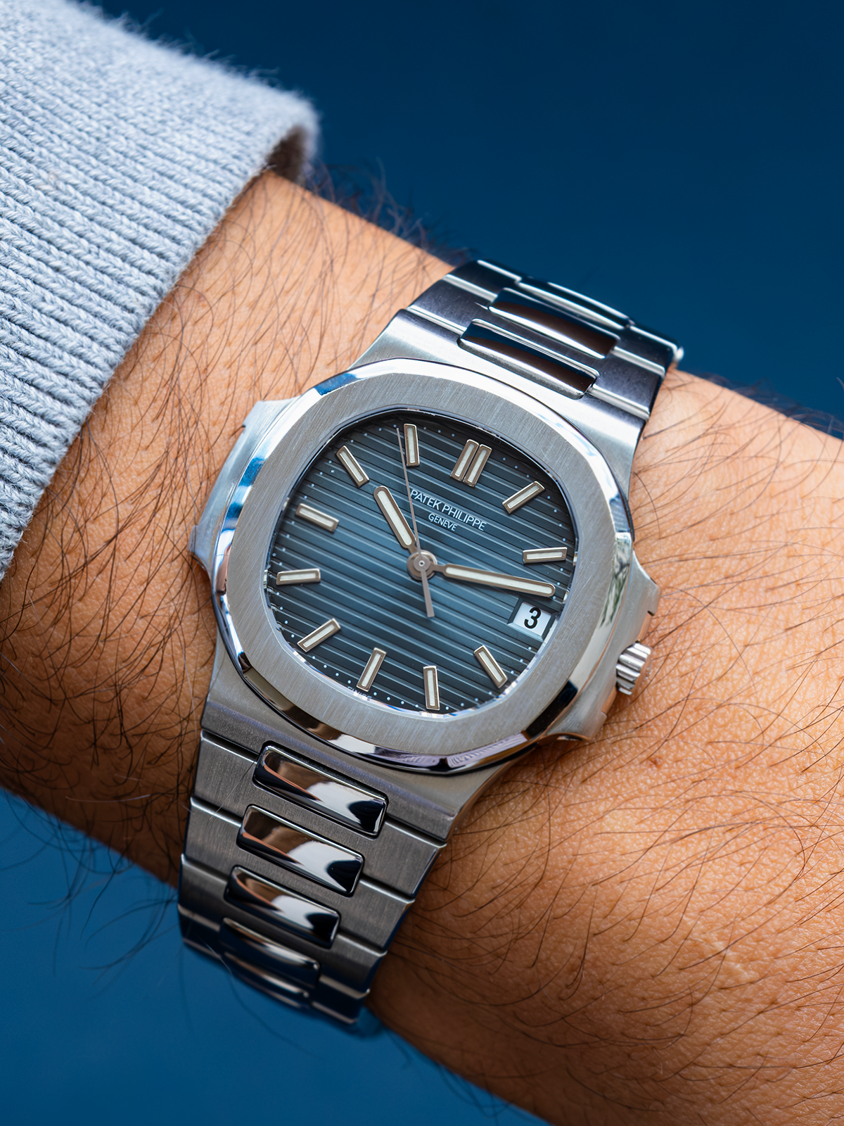 Silver watch on a wrist with a blue background