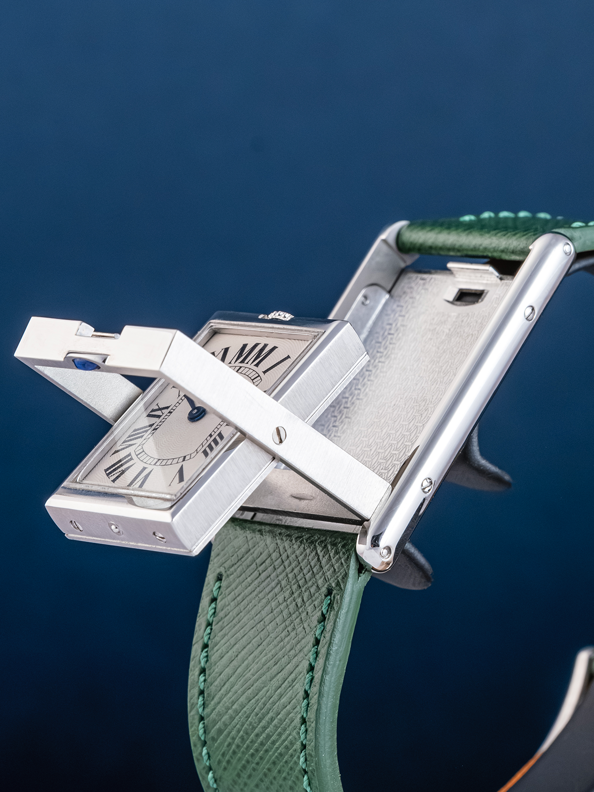 Close-up of a silver watch with a green strap against a dark blue background