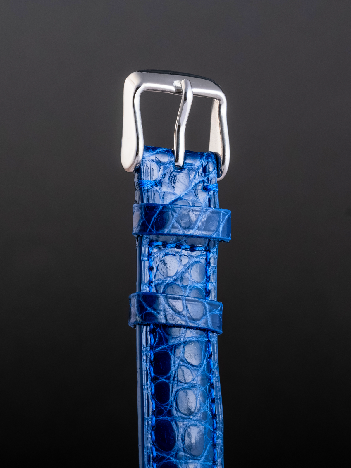 Blue textured watch strap with silver buckle on a dark background