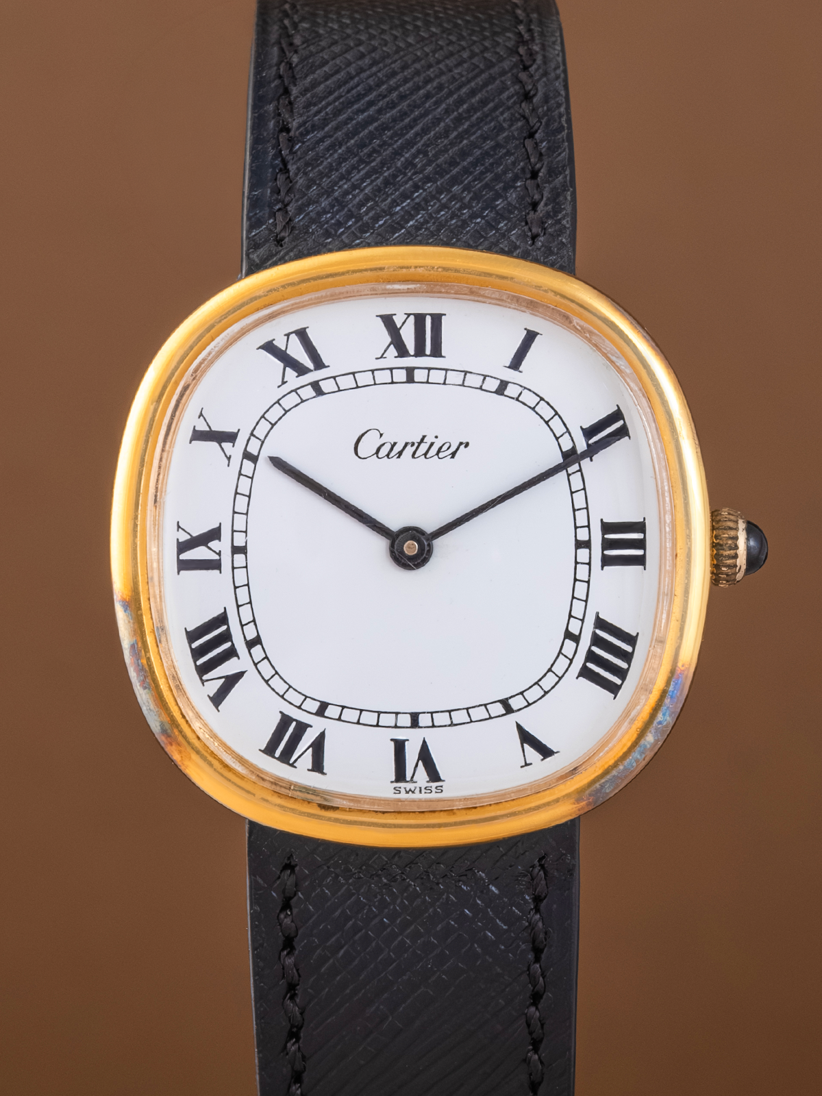 Cartier watch with gold case and black leather strap on a brown background