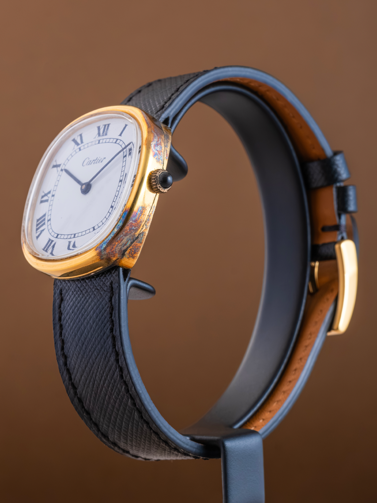 Luxury watch with gold case and black leather strap on a brown background