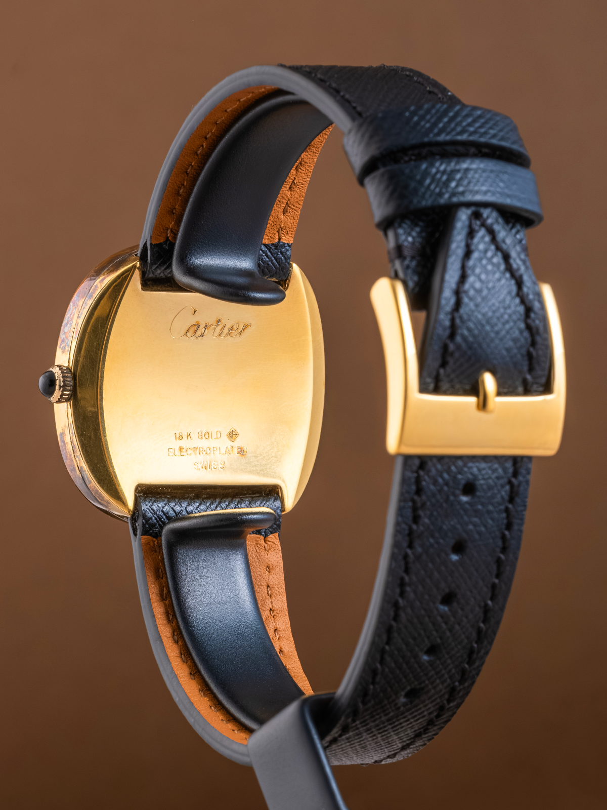 Cartier watch with gold case and black leather strap on a brown background