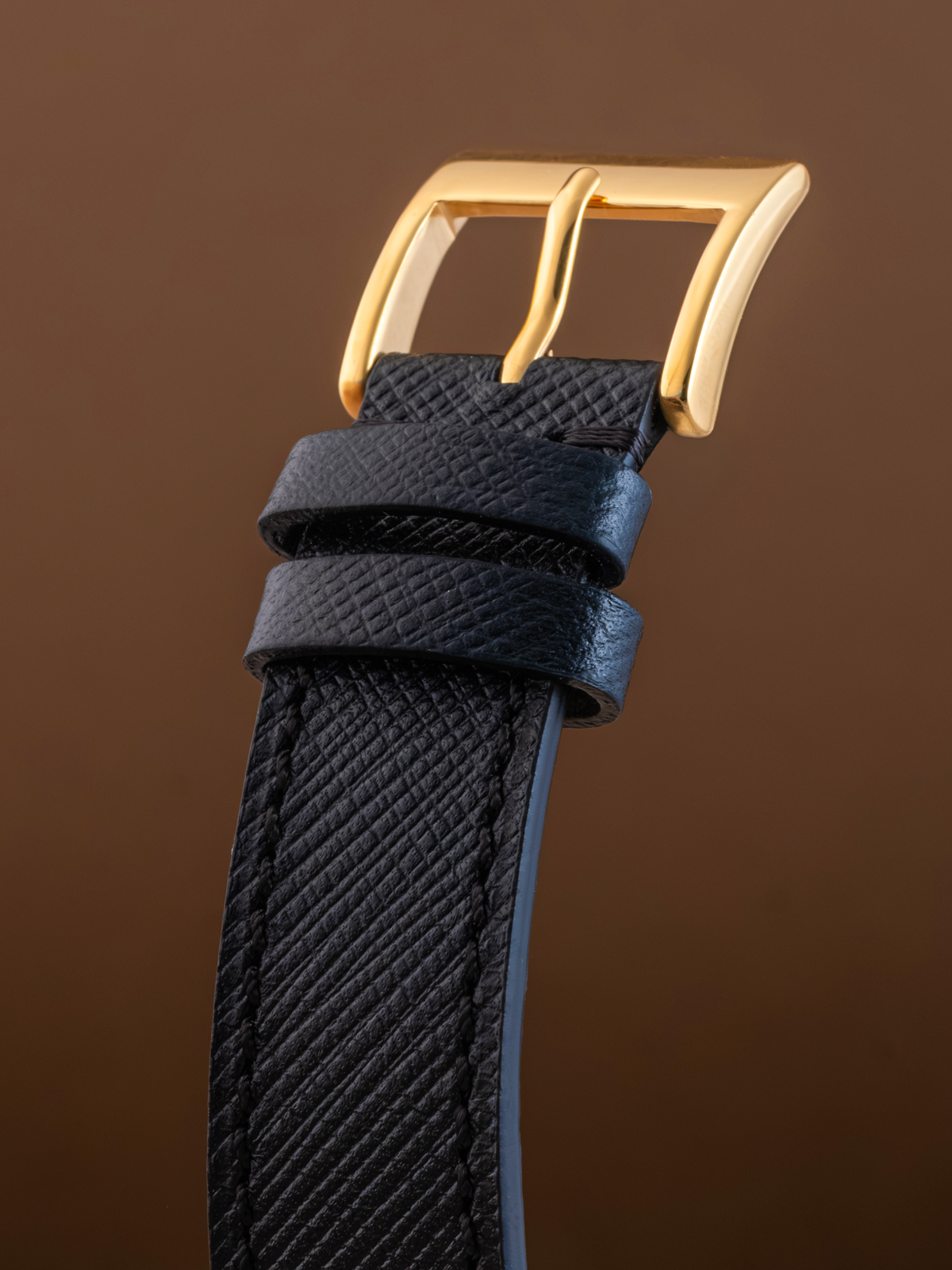 Black textured watch strap with a gold buckle on a brown background