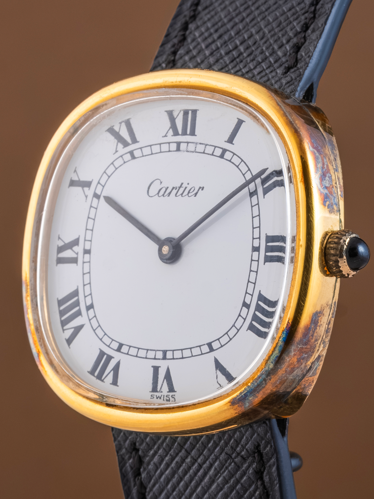 Cartier watch with gold case and black leather strap on a brown background