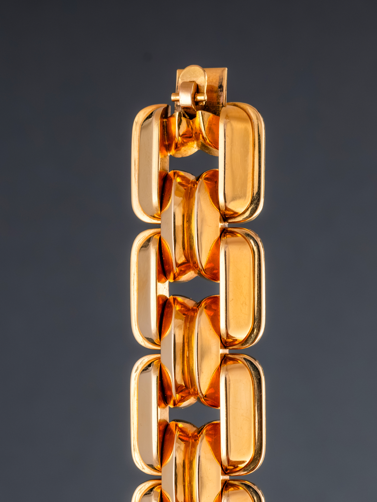 Gold chain bracelet on a reflective surface with a dark background
