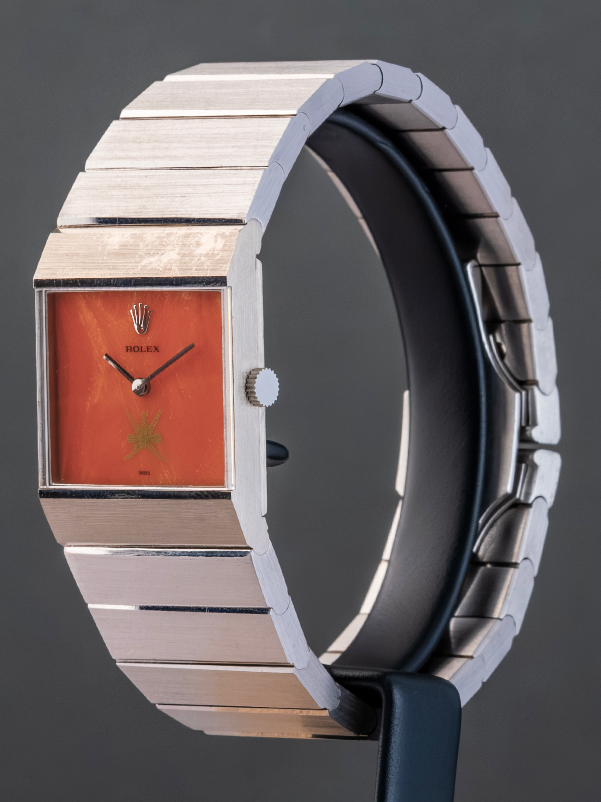 Luxury watch with a metallic band and orange face on a dark background