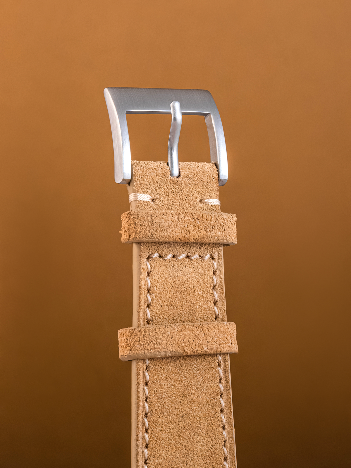 Brown leather watch strap with silver buckle on a brown background