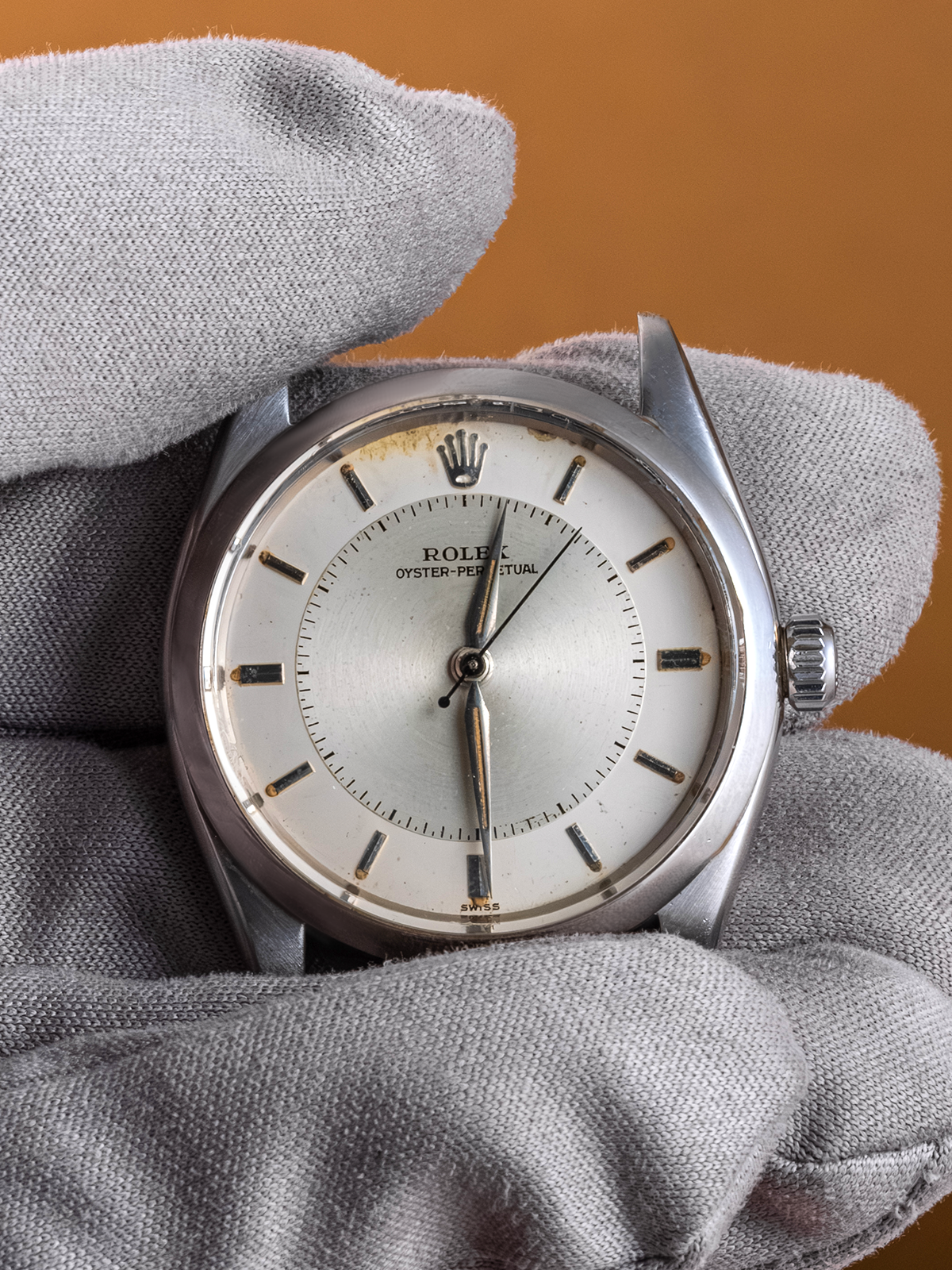Rolex watch held in gray gloves against a brown background