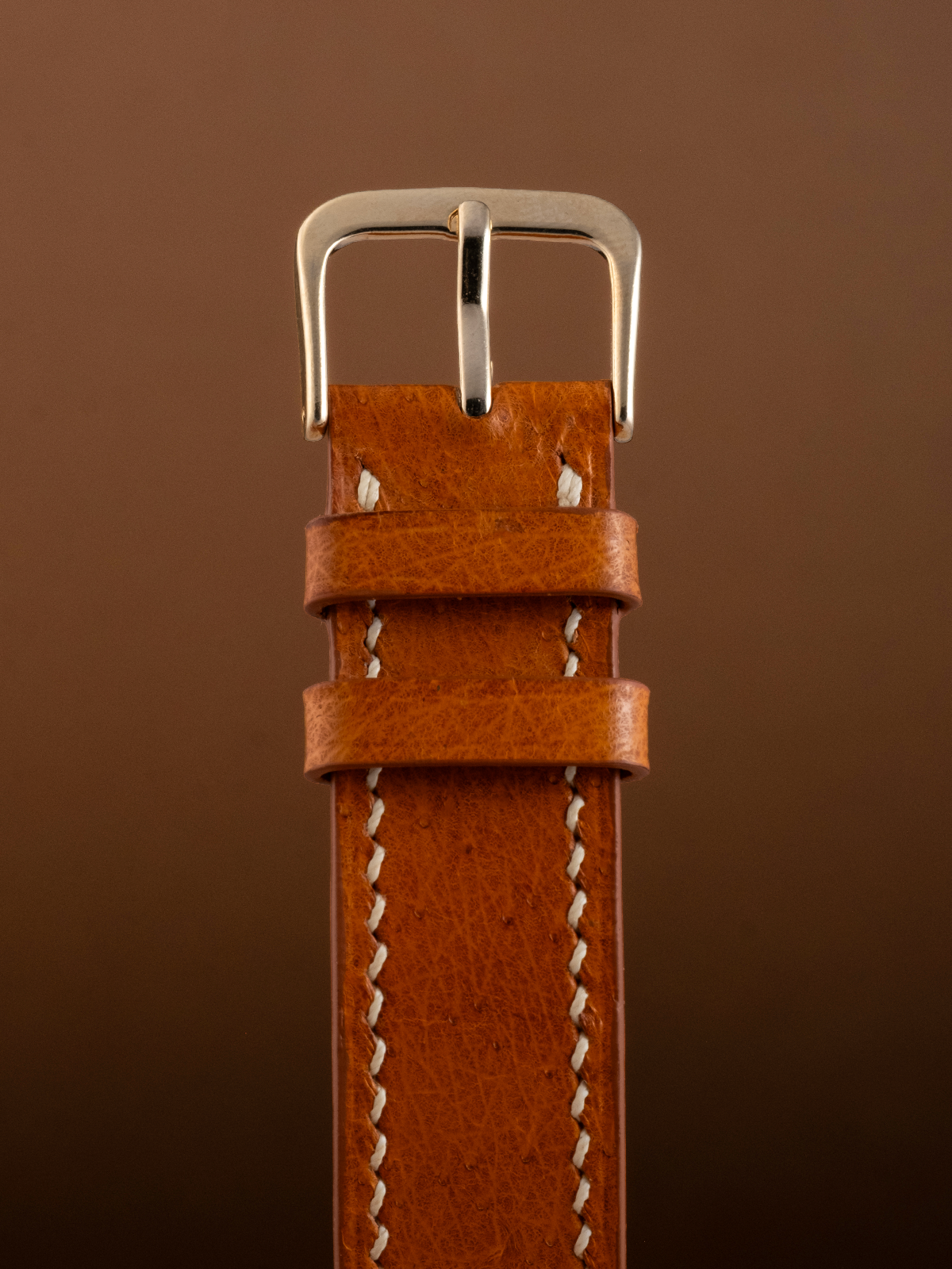 Brown leather watch strap with silver buckle on a brown background