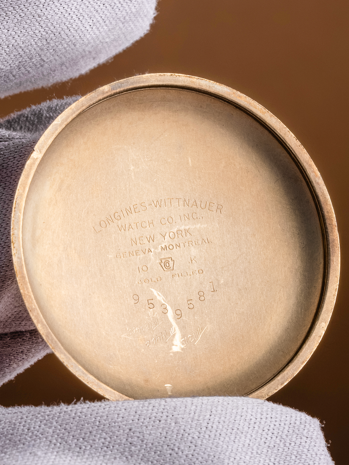 Close-up of a watch case with 'Longines Whittaker' engraving on a brown background