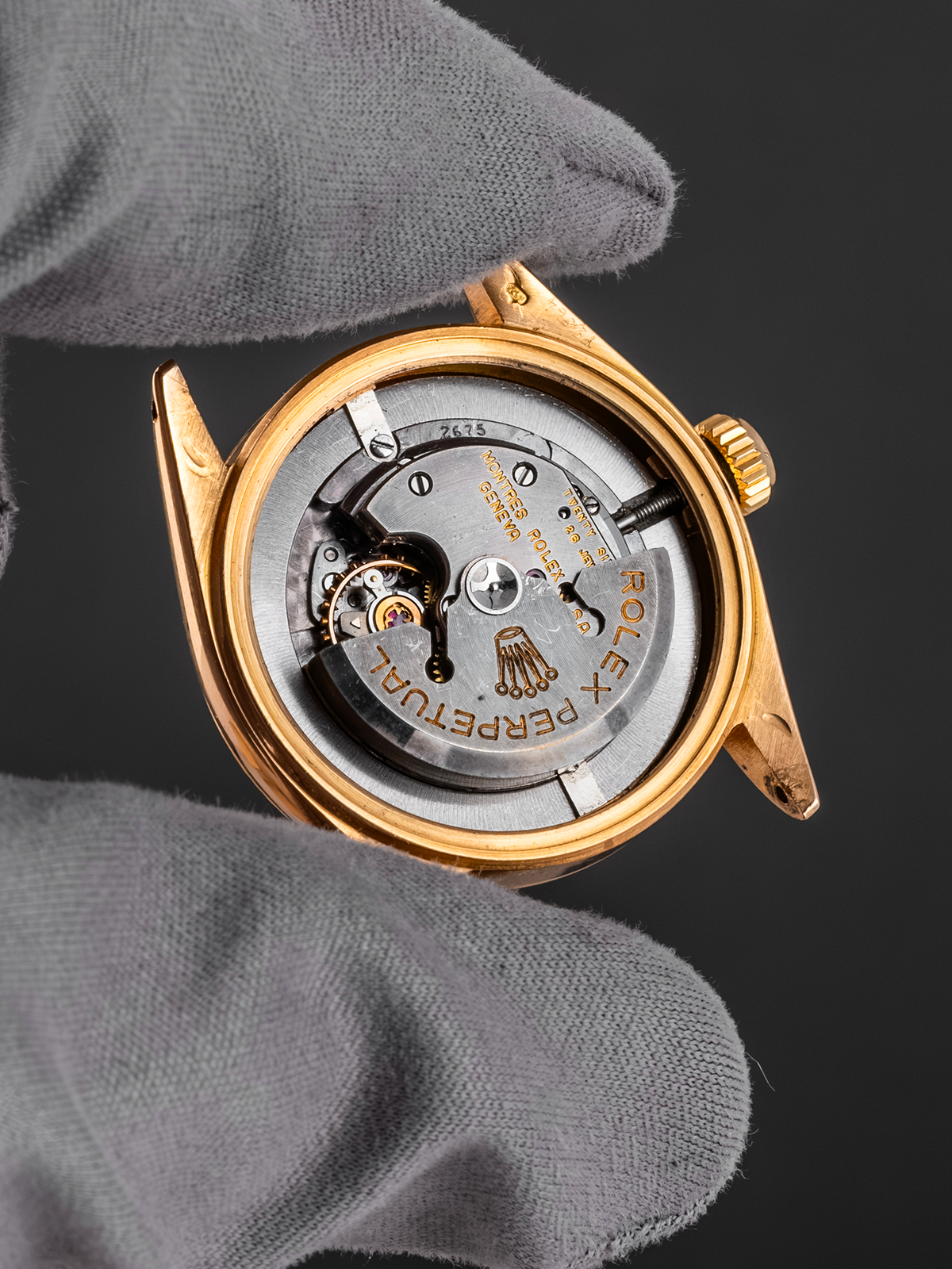 Close-up of a gold watch with visible mechanism held by a gray glove against a dark background
