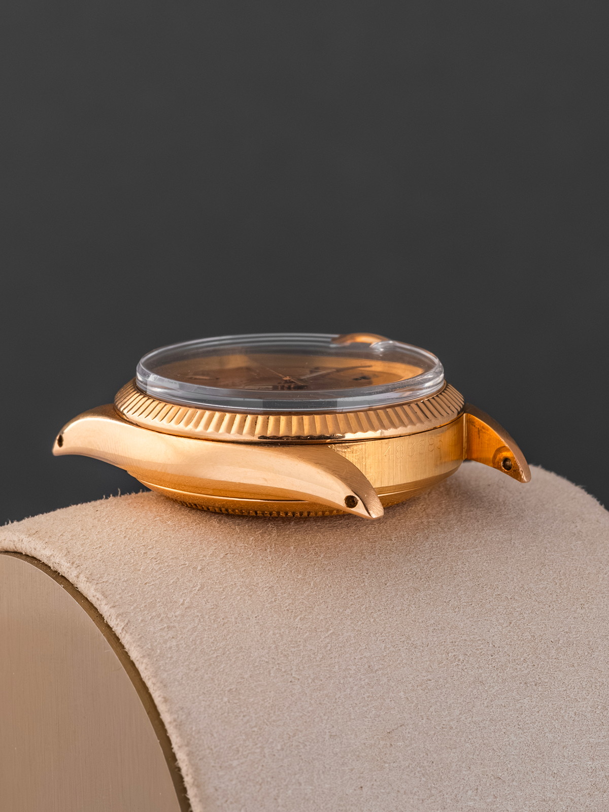 Gold wristwatch on a beige cushion with a dark background