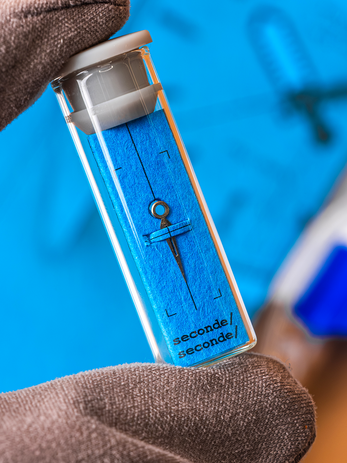 Blue glass bottle with silver cap held by a brown hand against a blue background