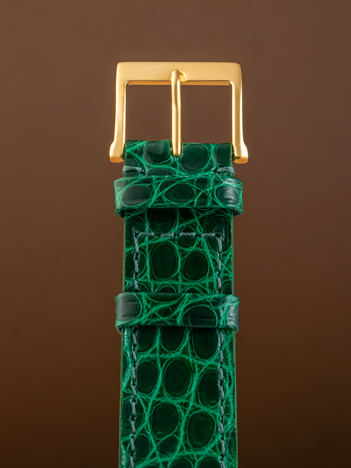 Green crocodile skin watch strap with gold buckle on a brown background