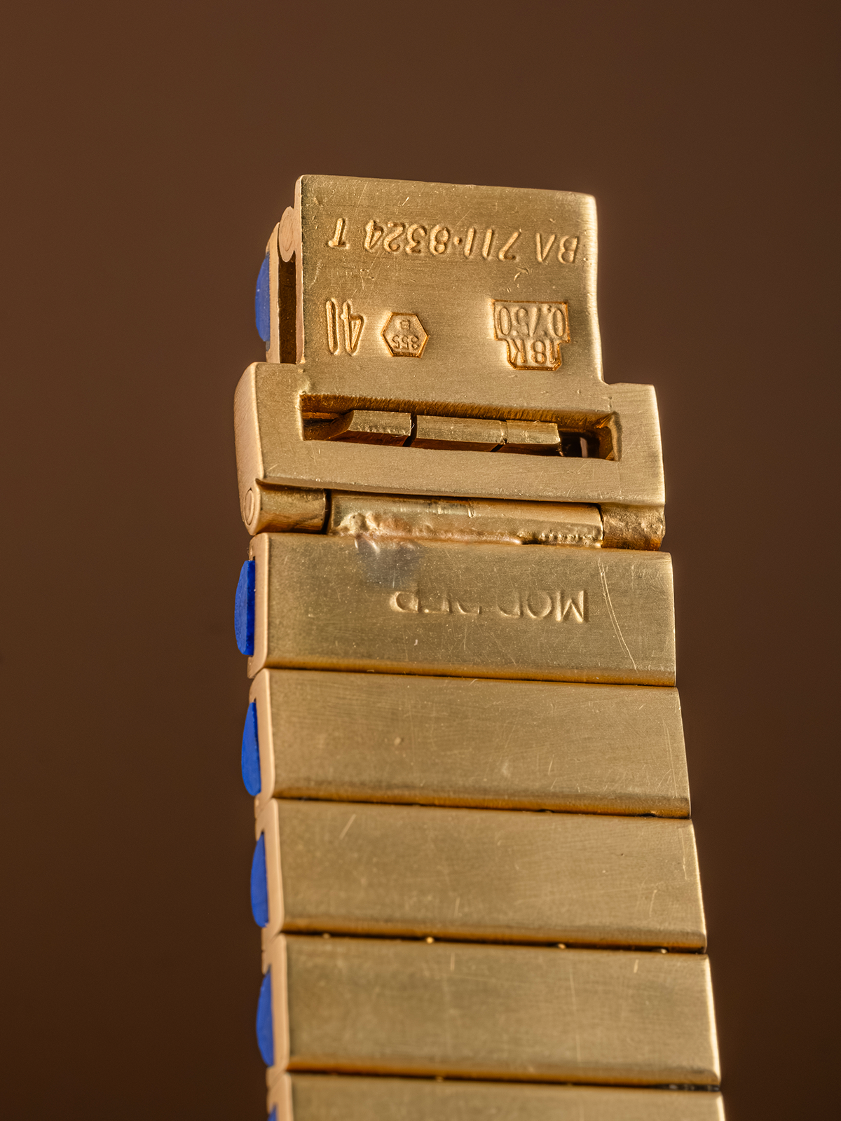 Gold watch band with brand name on a brown background