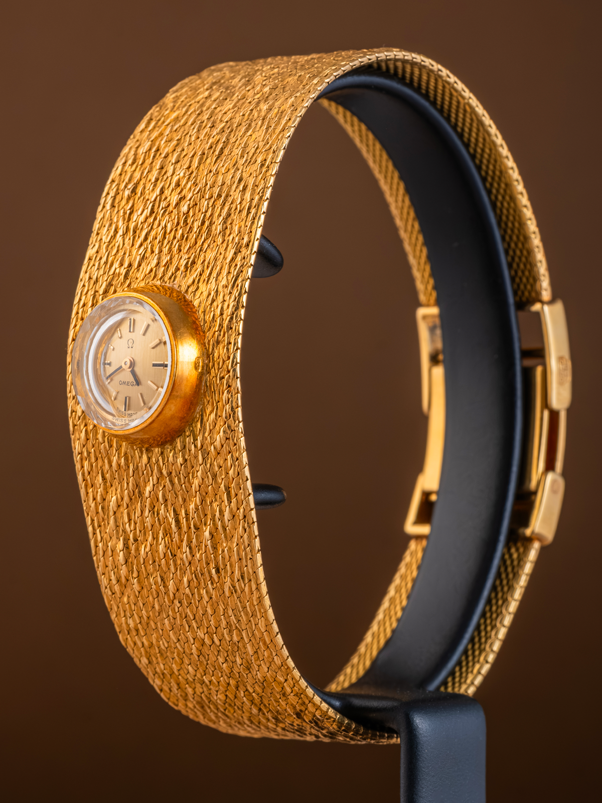Gold and black watch with textured band on a brown background