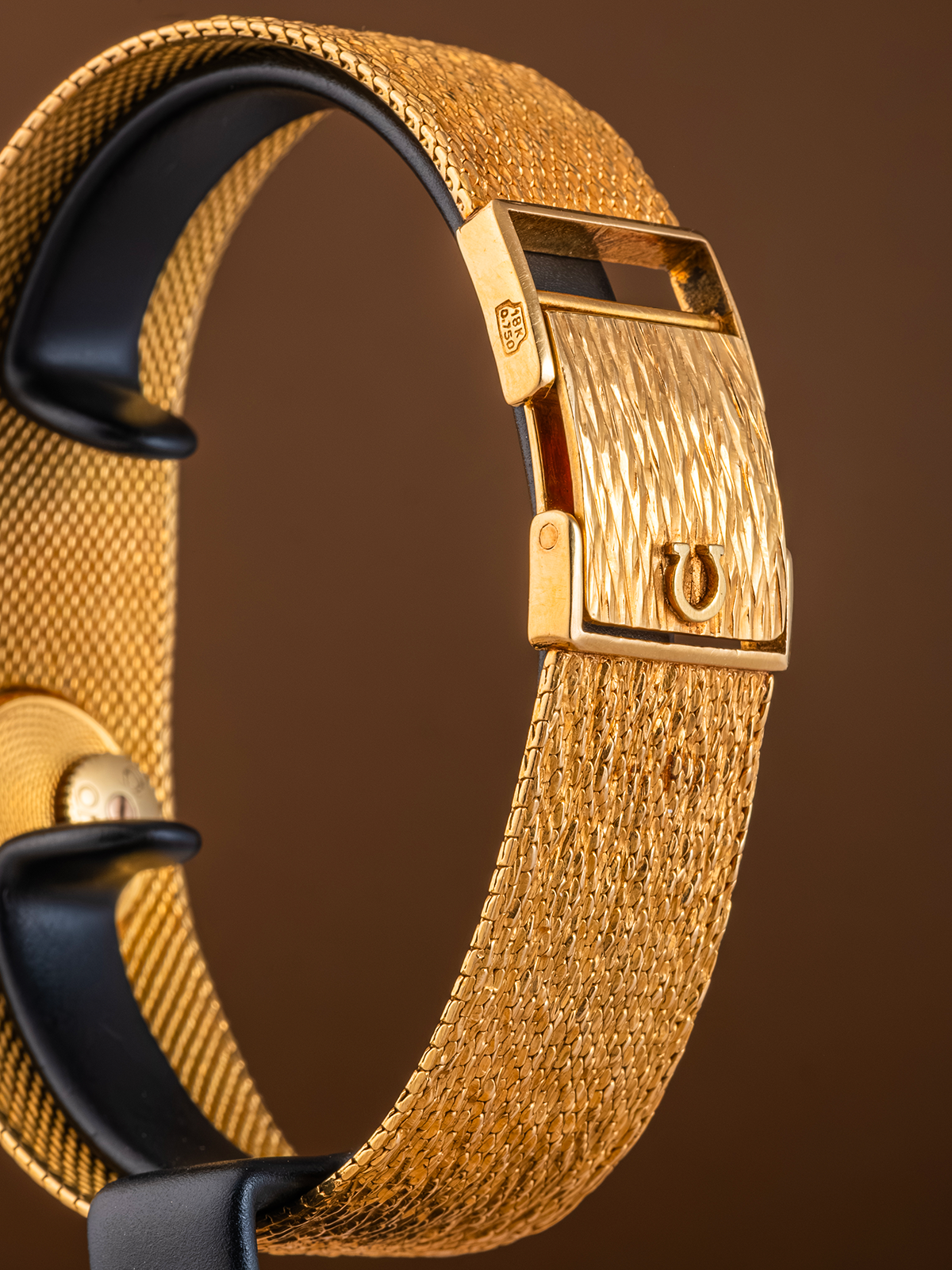 Close-up of a gold watch strap with a brown background