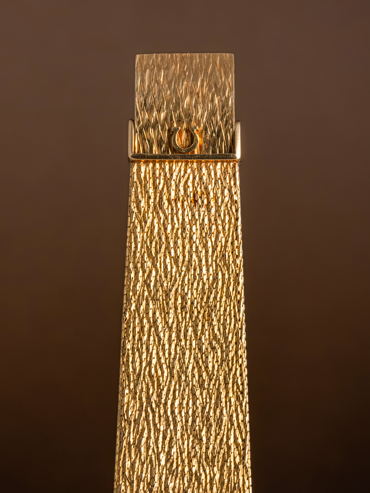 Gold textured object with a brand logo on a brown background