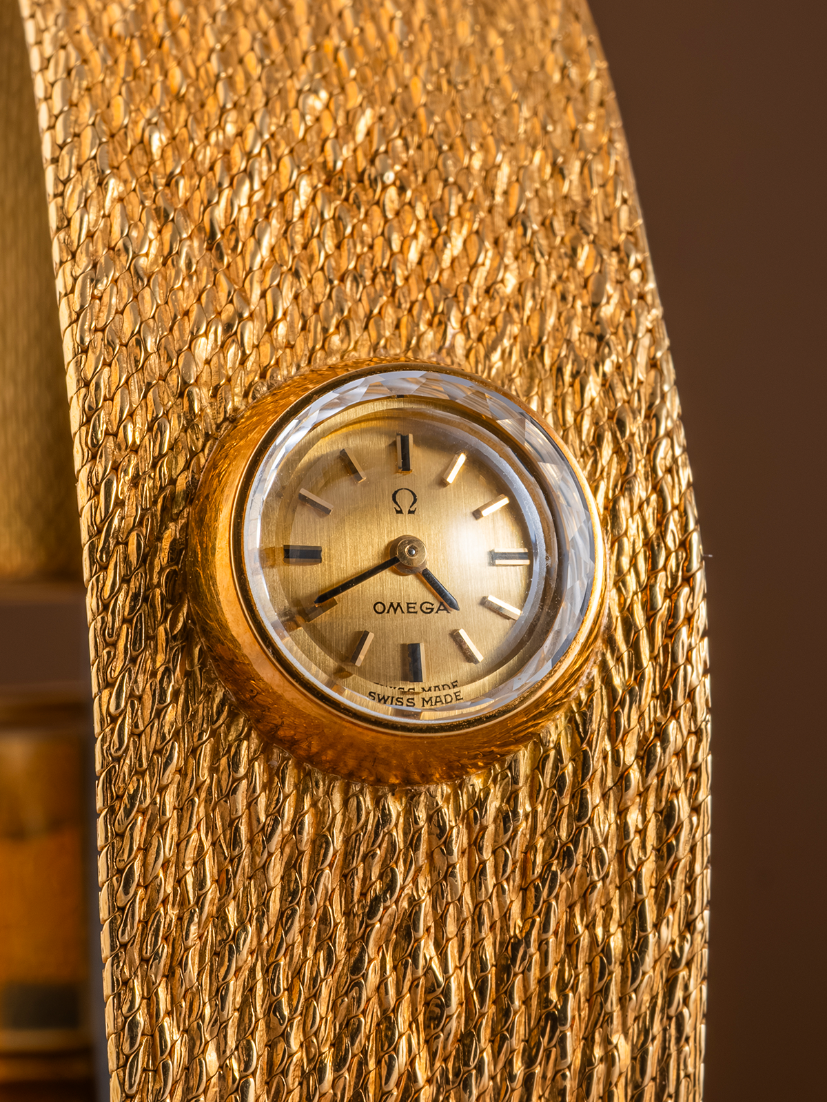 Gold textured object with a small clock face on a brown background