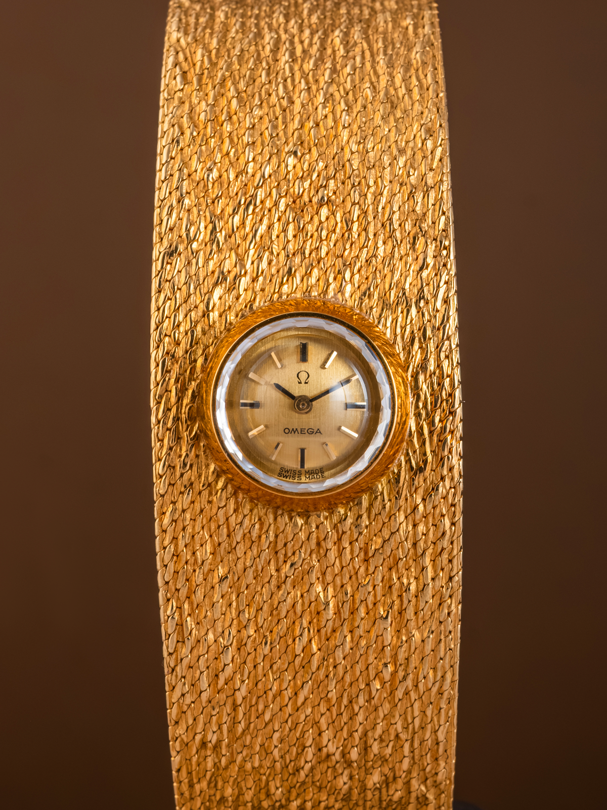 Gold wristwatch with a textured band on a brown background