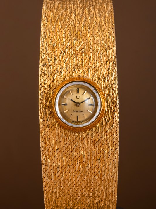 Gold wristwatch with a textured band on a brown background