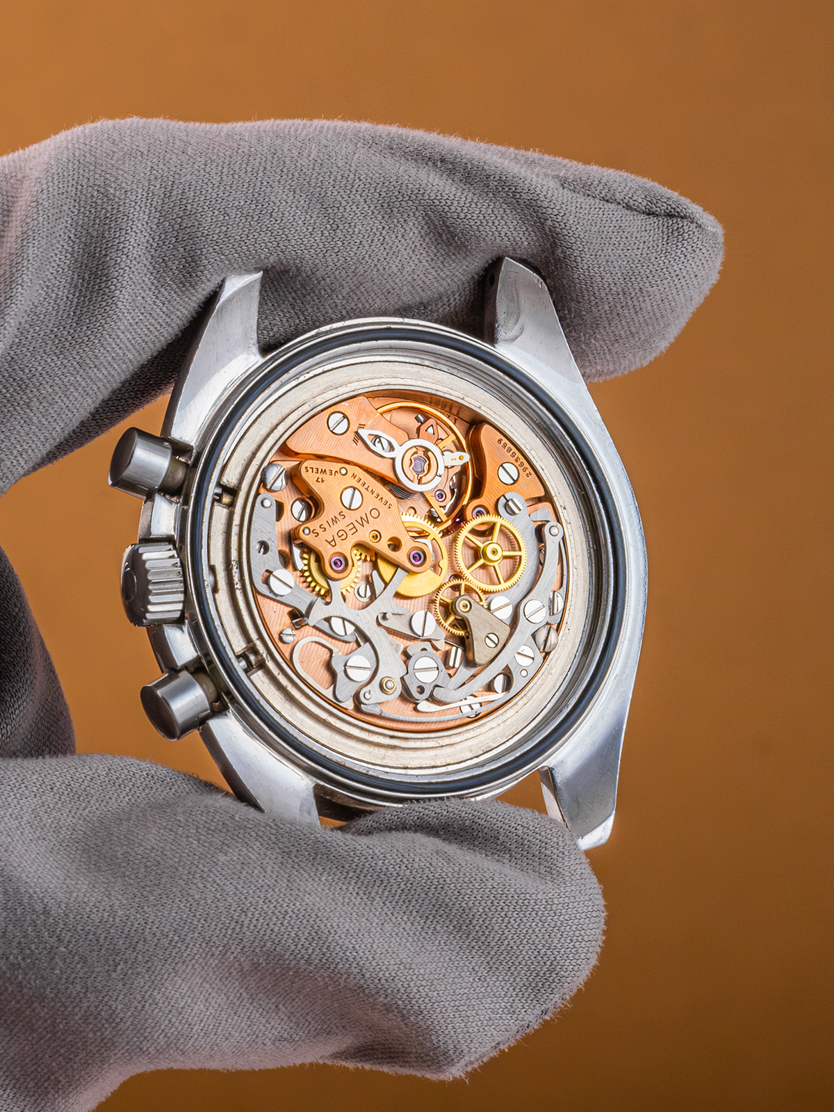 Close-up of a mechanical watch with visible gears held by a gloved hand against a brown background
