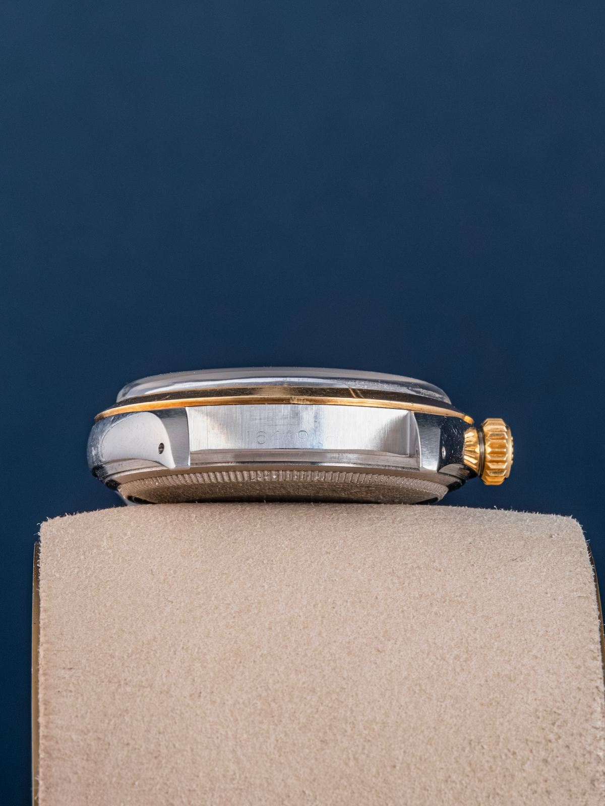 Close-up of a silver and gold watch on a beige stand with a dark blue background