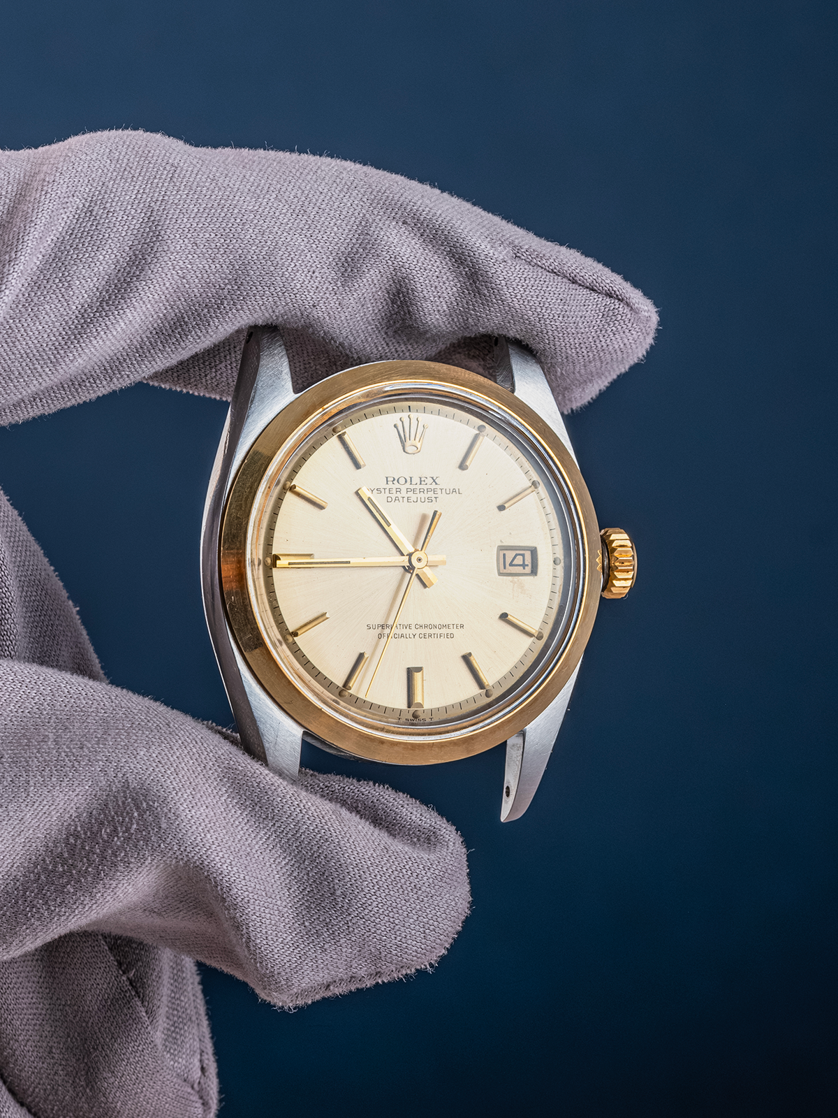 Rolex watch held by a gloved hand against a dark blue background