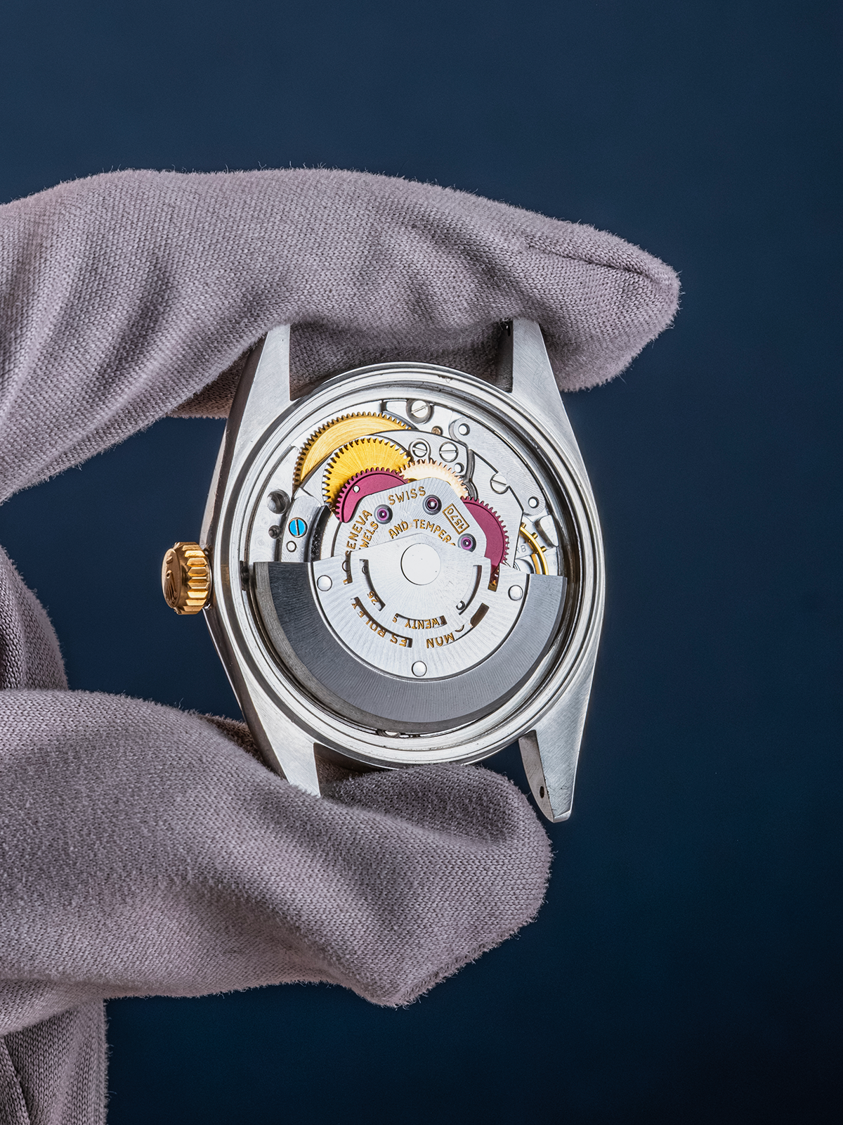 Watch mechanism held by a gloved hand against a dark background