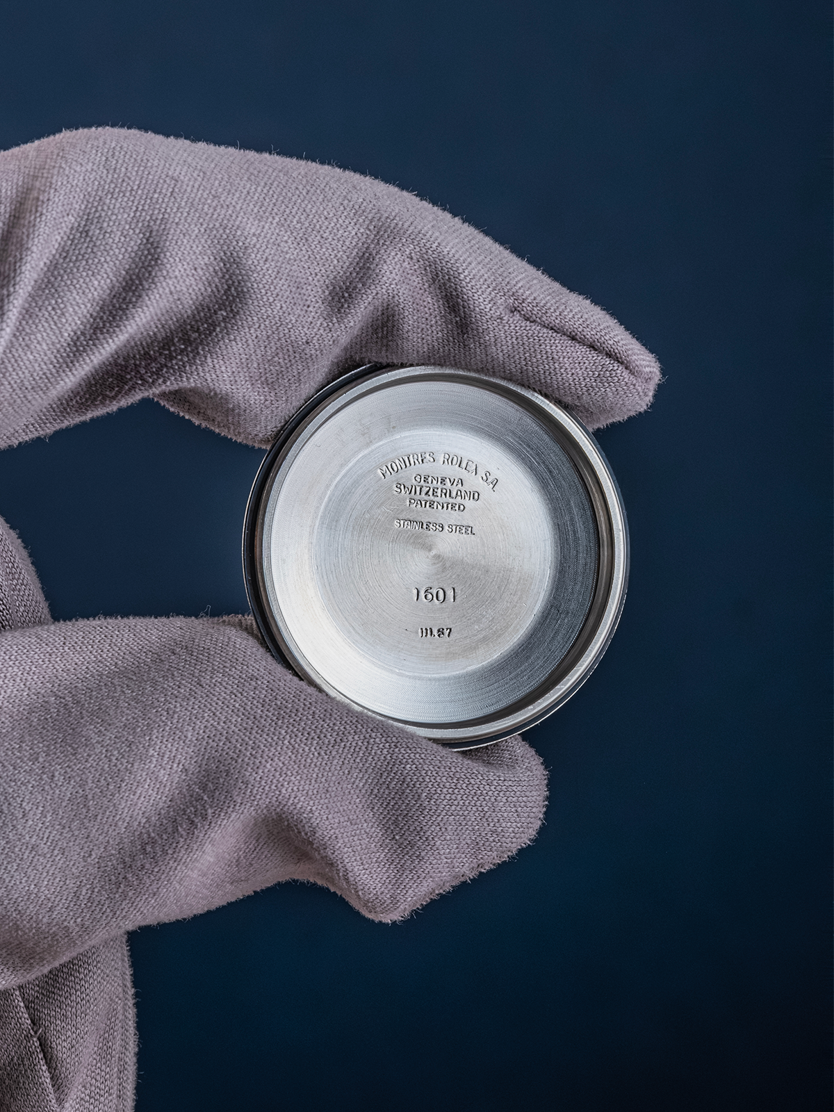 Silver watch case with brand engraving held by a gloved hand against a dark background