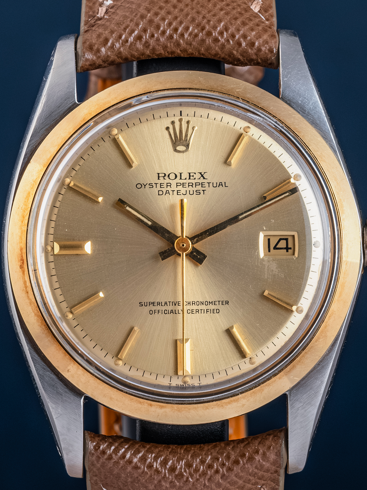 Rolex watch with gold face and brown leather strap on a dark background