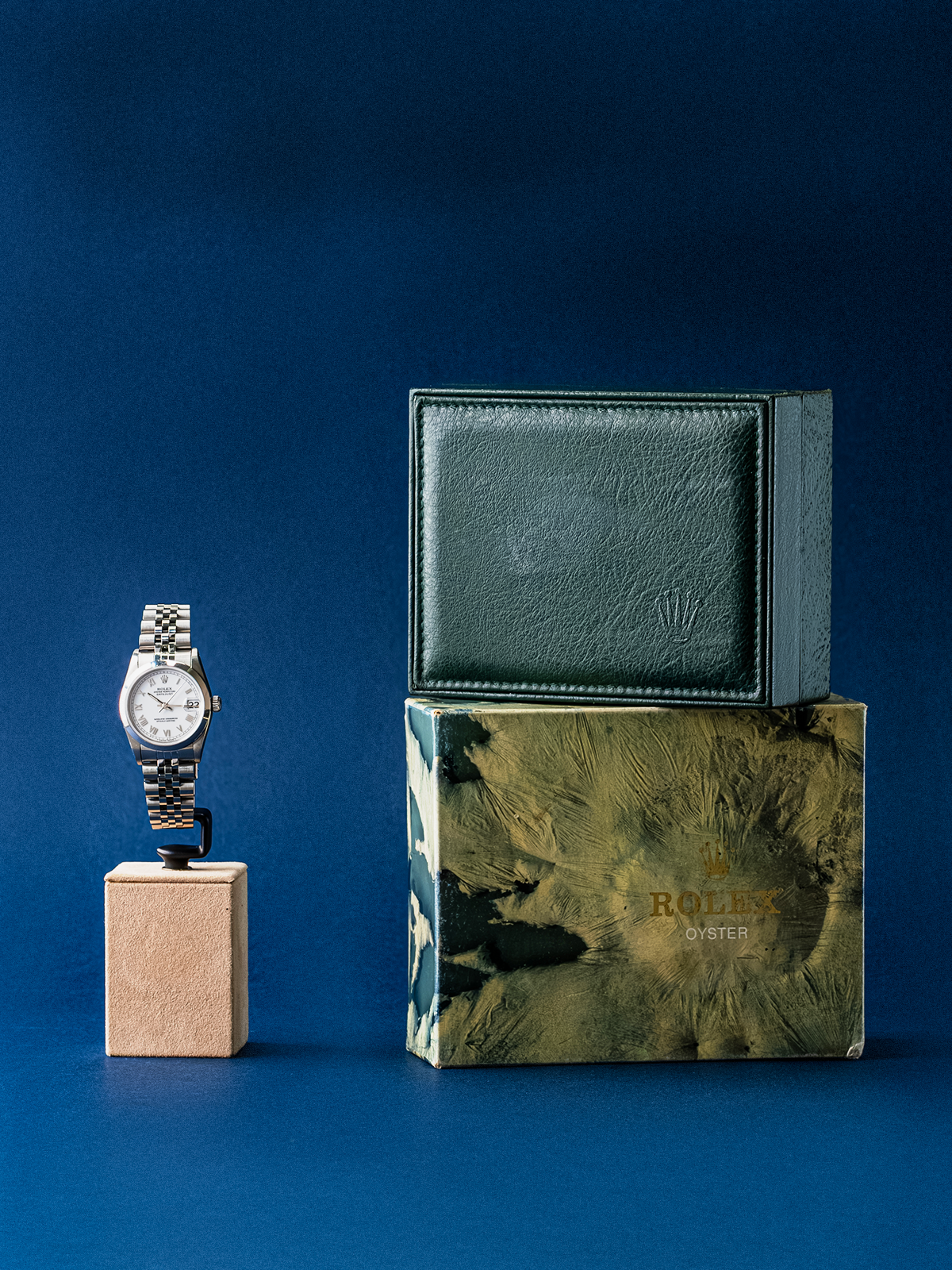 Rolex watch on a stand with a branded box against a blue background