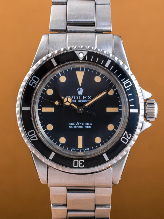 Rolex watch with black dial and silver metal bracelet on a brown background