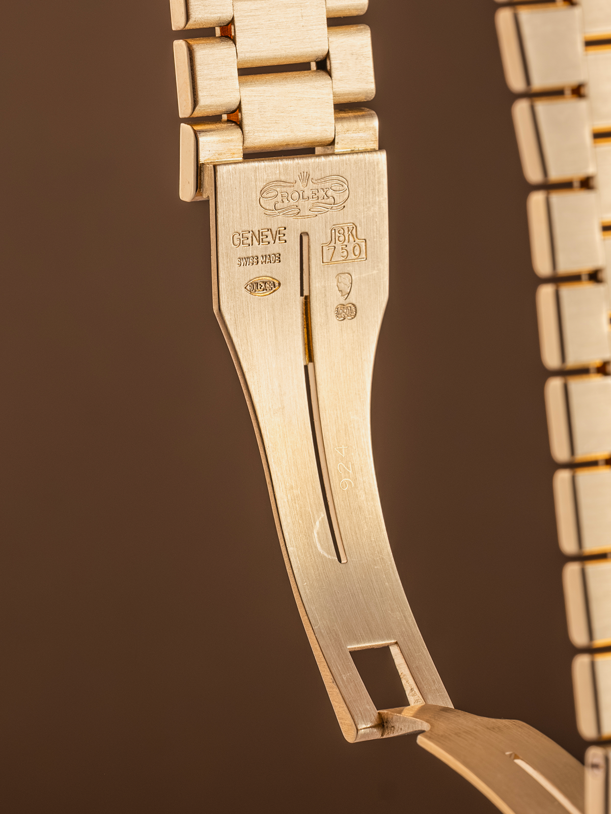 Close-up of a gold watch strap with Rolex branding on a brown background