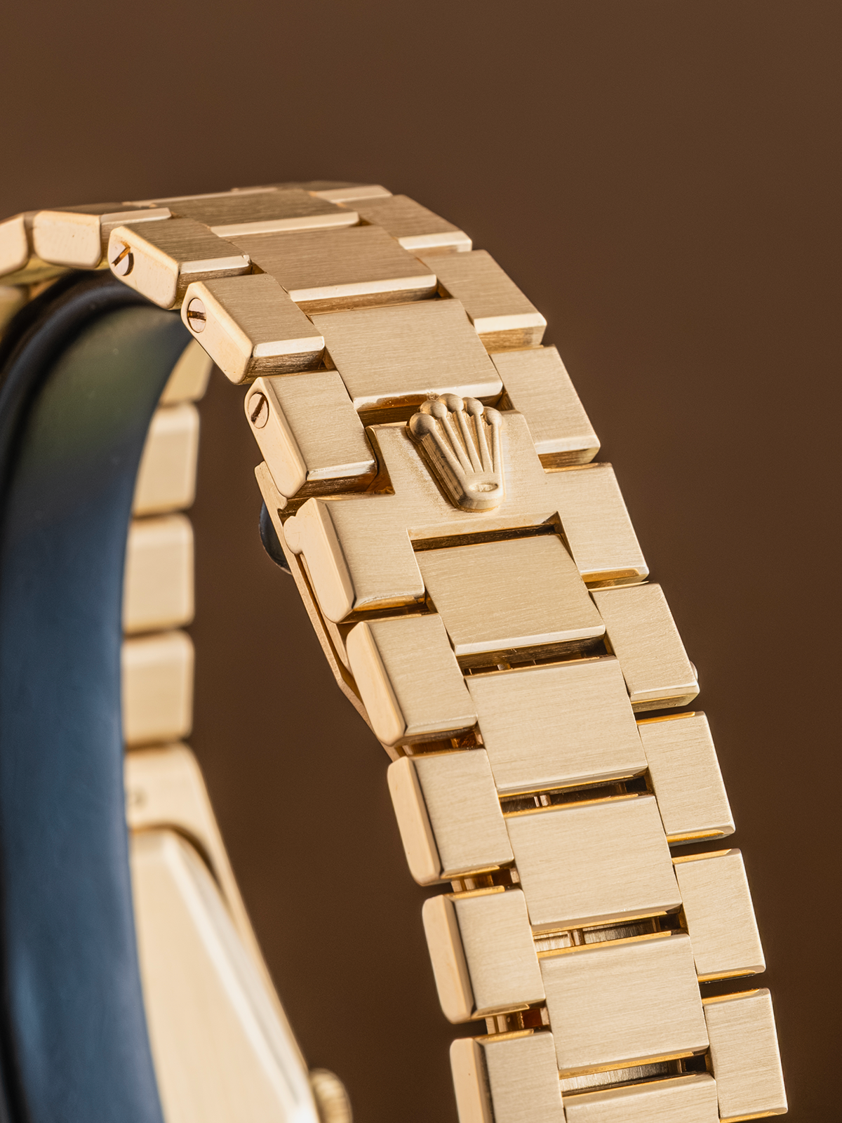 Gold watch strap with Rolex logo on a brown background