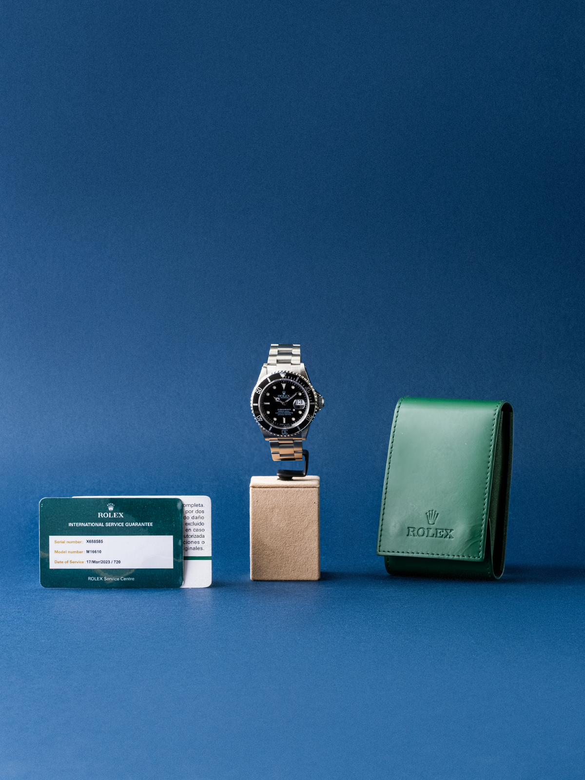 Rolex watch, card, and green leather case on a blue background