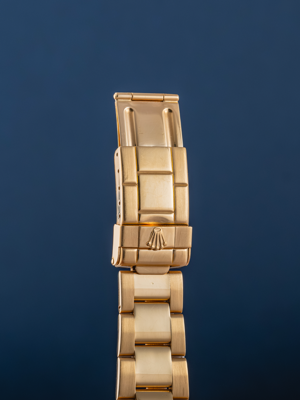 Gold watch strap with Rolex logo on a dark blue background