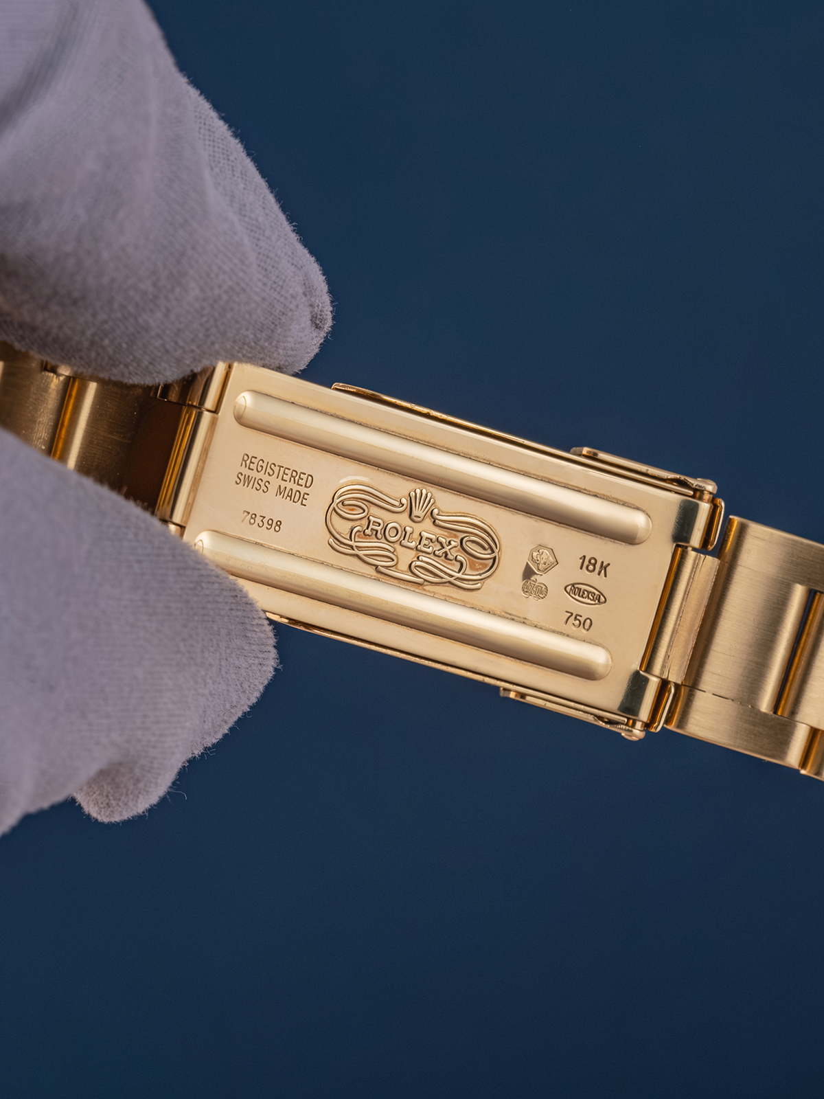 Gold watch band with a gloved hand holding it against a dark blue background