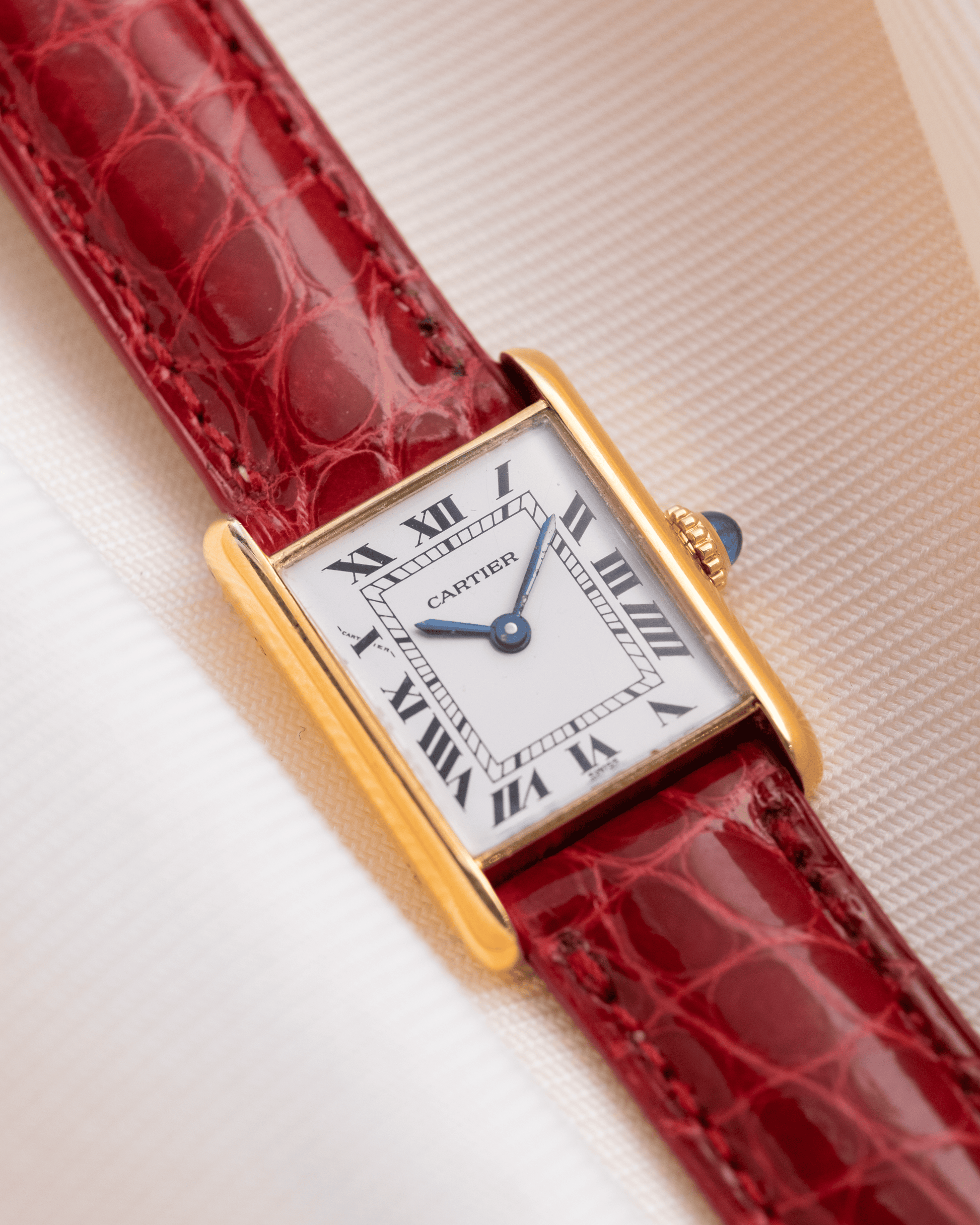 Cartier watch with red strap and gold case on a light background