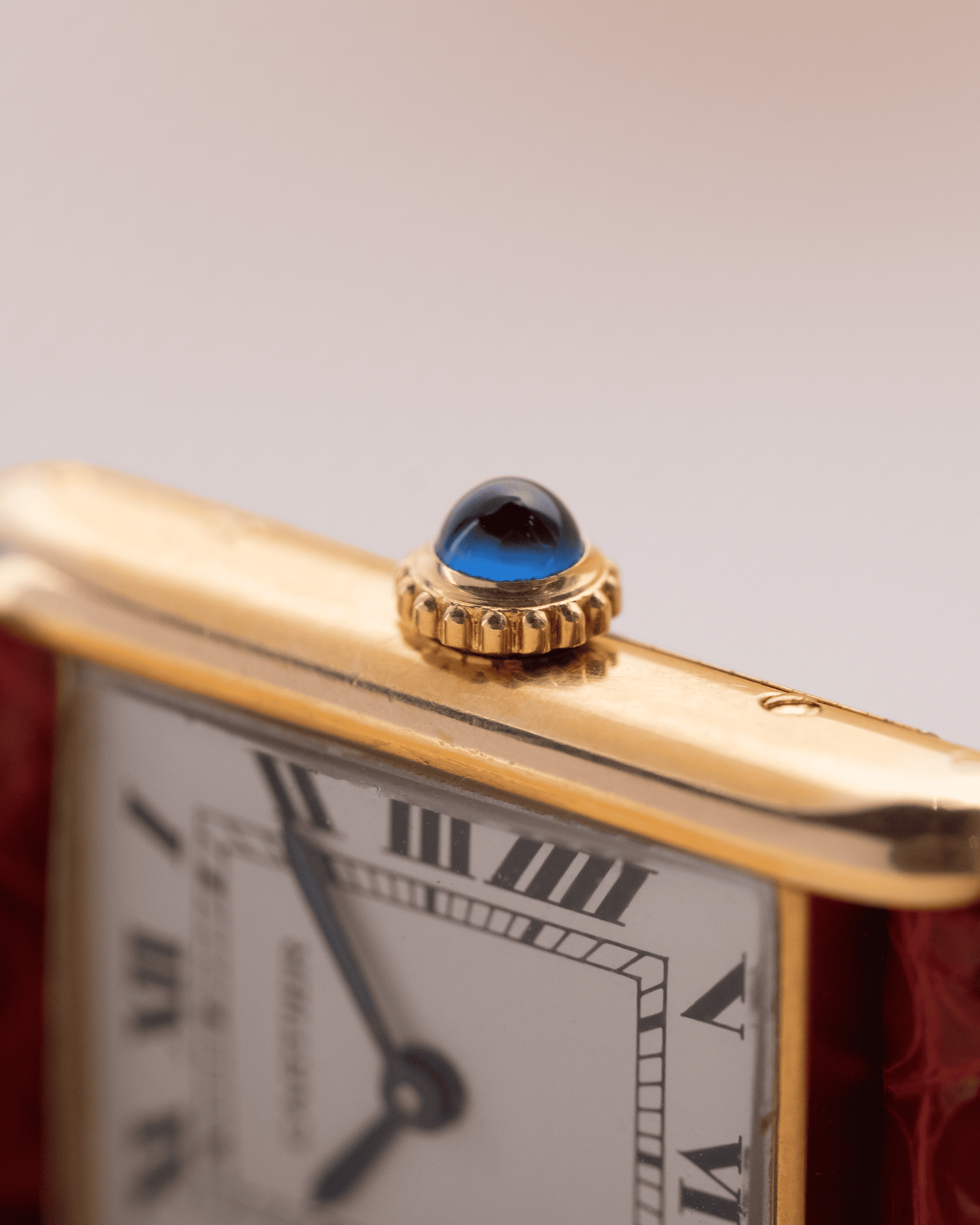 Close-up of a gold watch with a blue gemstone on a gray background
