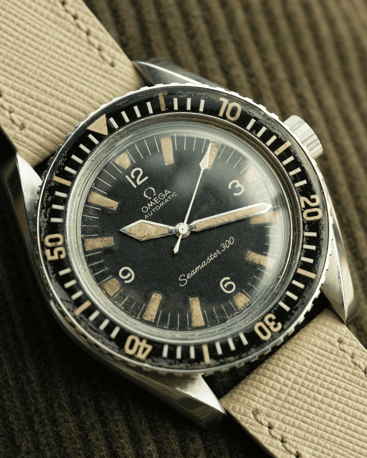 Vintage Omega watch with black dial and beige strap on a textured background