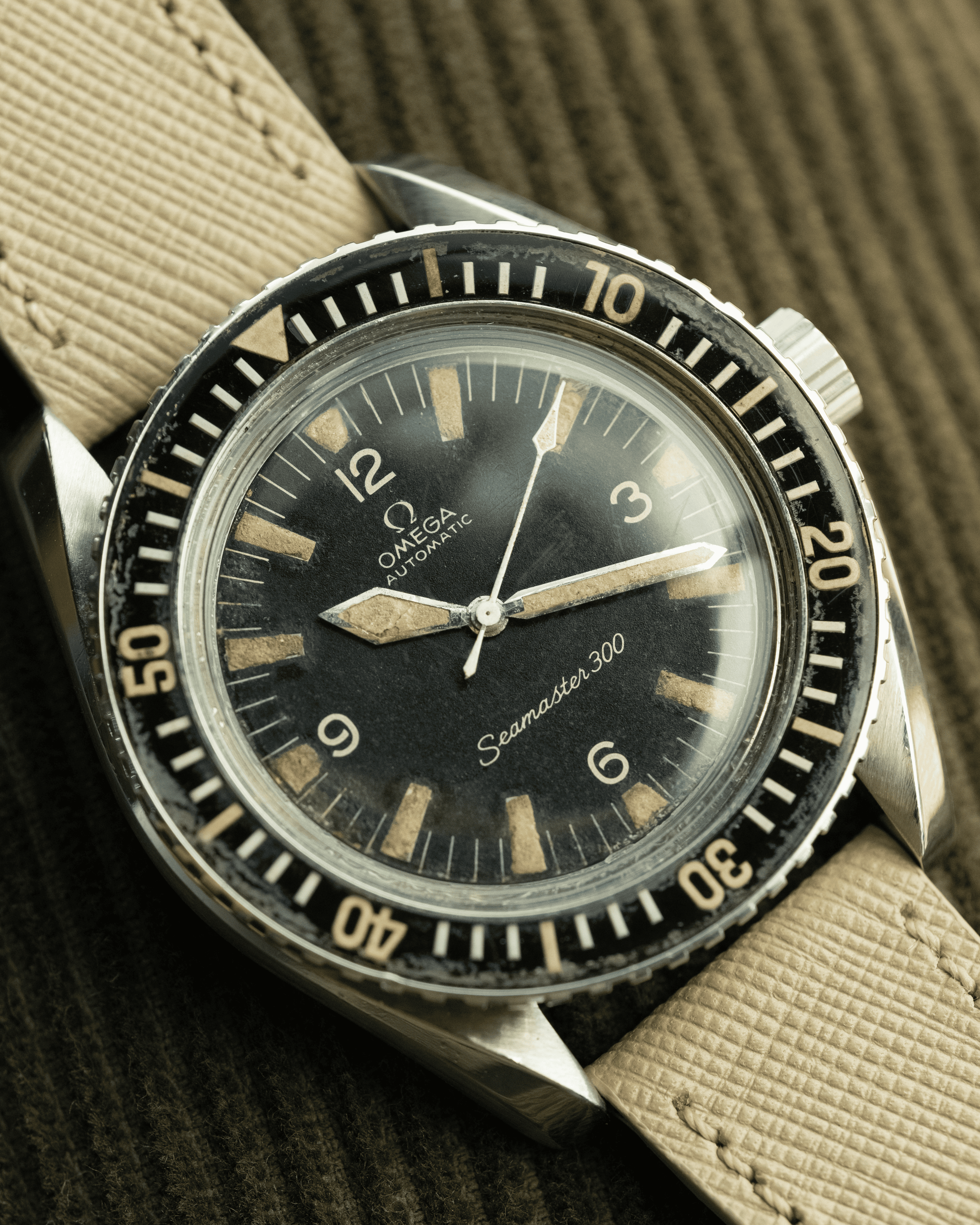 Vintage Omega watch with black dial and beige strap on a textured background