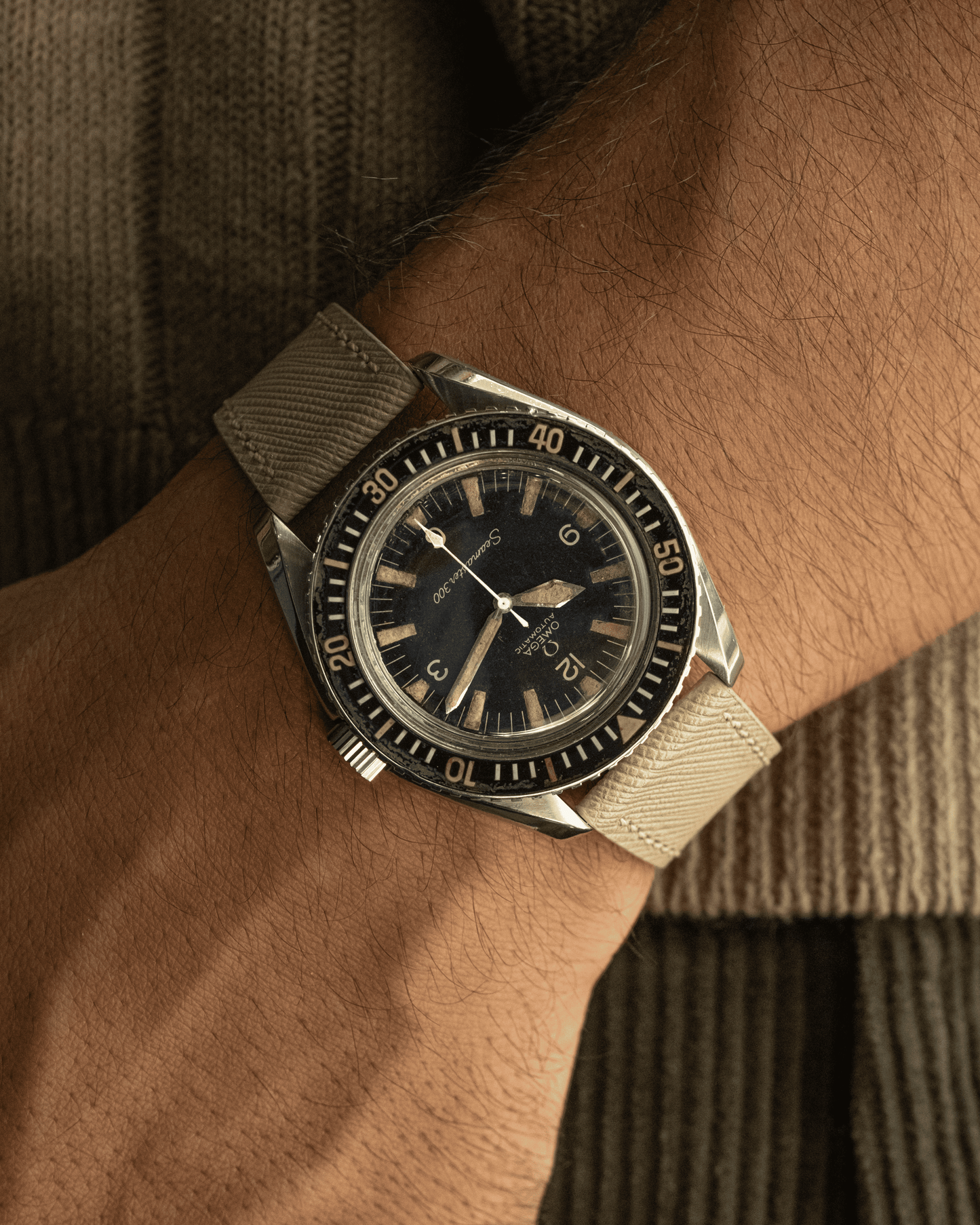 Vintage-style watch with beige strap on a wrist against a brown textured background