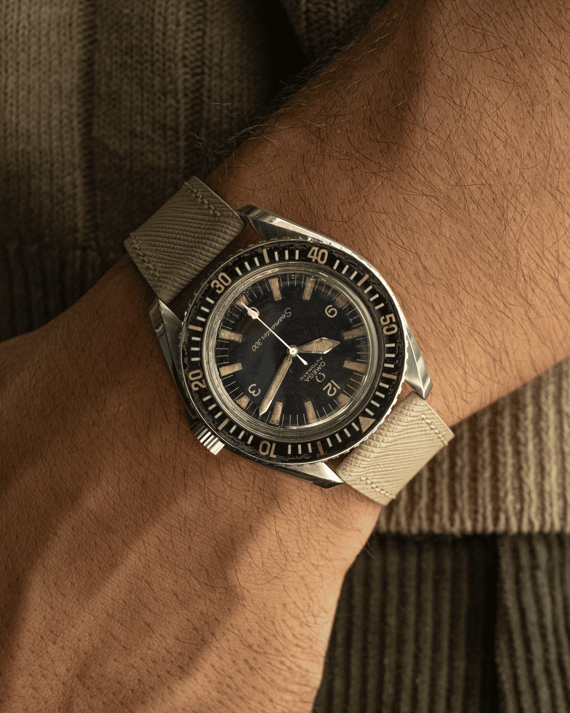 Vintage-style watch with beige strap on a wrist against a brown textured background