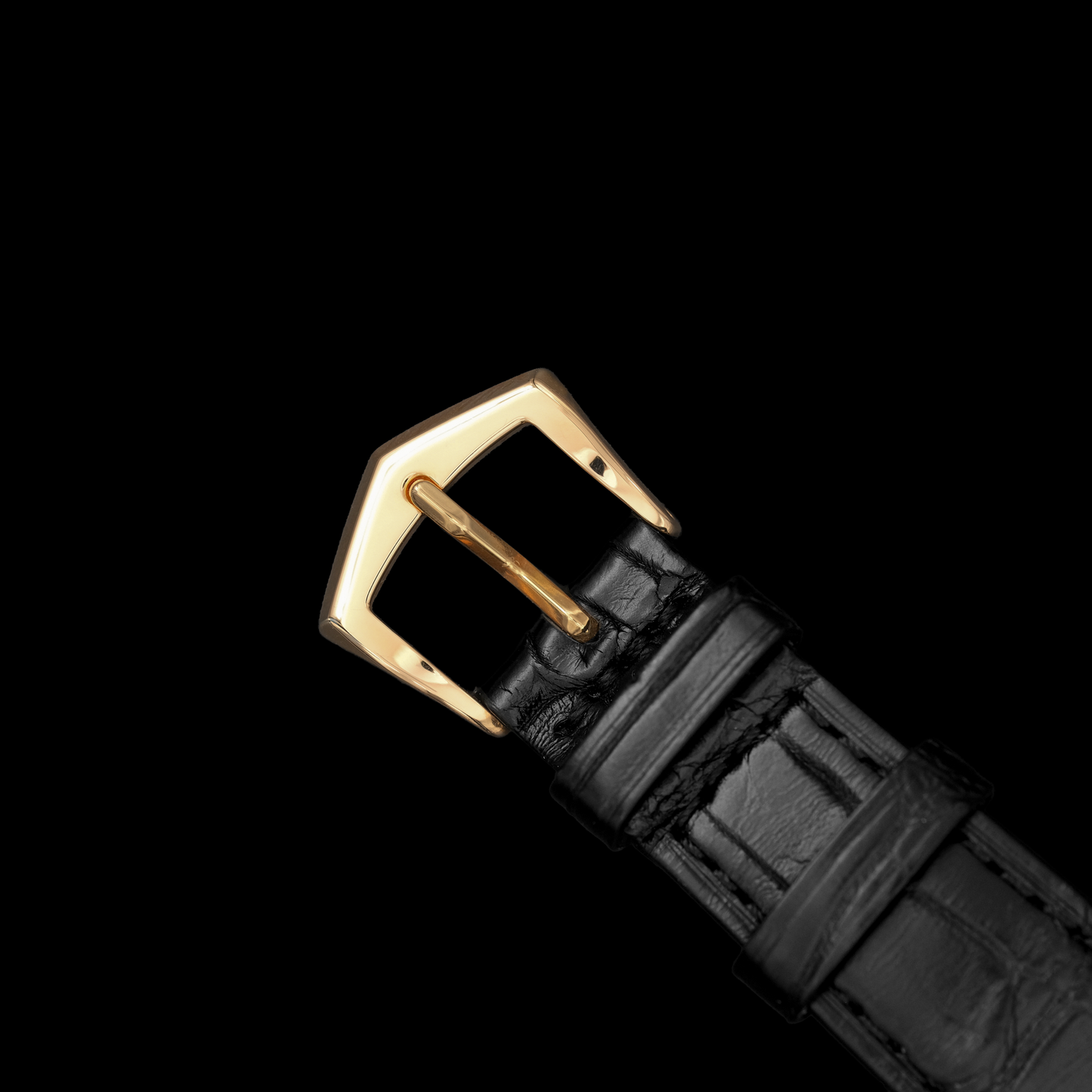 Black leather watch strap with a gold buckle on a black background